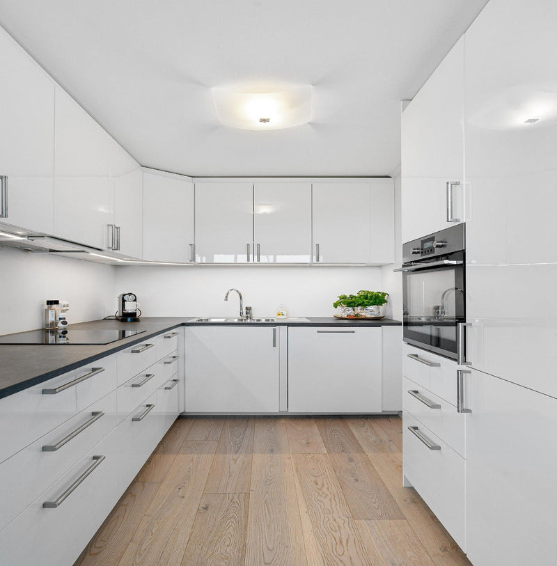 Modern kitchen with white cabinets, black countertops, and wooden flooring.